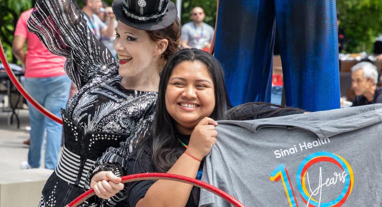 A circus performer with hula hoops posing next to a health-care provider holding up a Sinai Health t-shirt. 